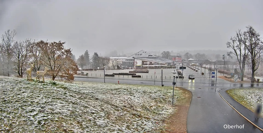 Oberhof bei bedecktem Himmel, Schnee auf den Wiesen, nasse Fahrbahn.